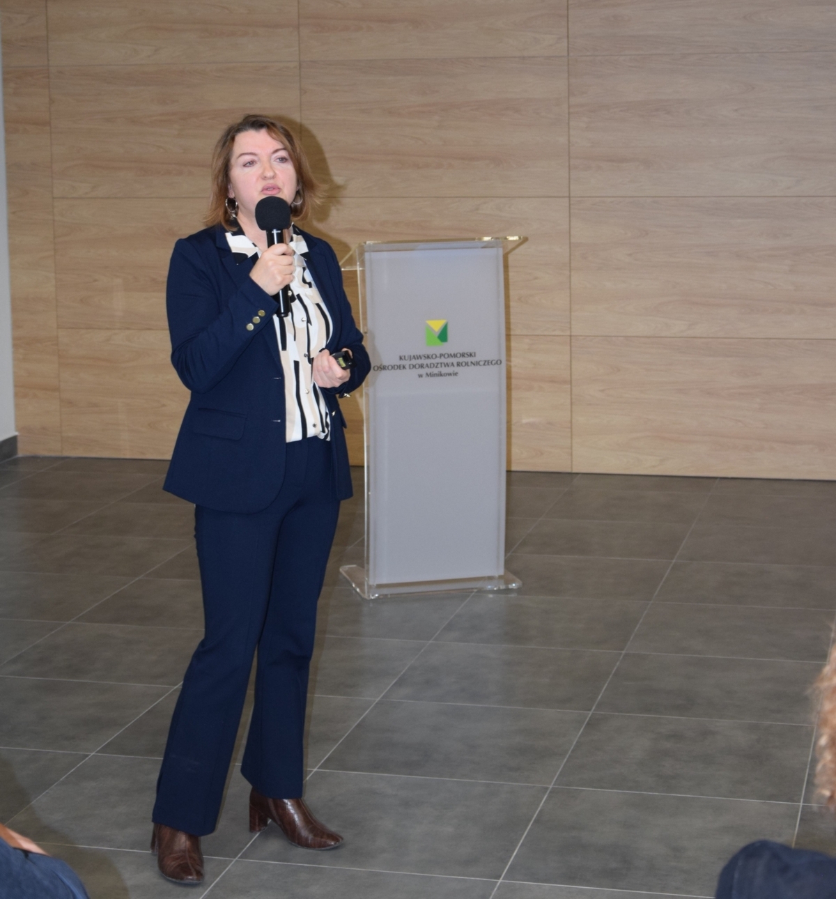 dyrektor SDOO Beata Kaliska stojąca z mikrofonem na tle logo KPODR