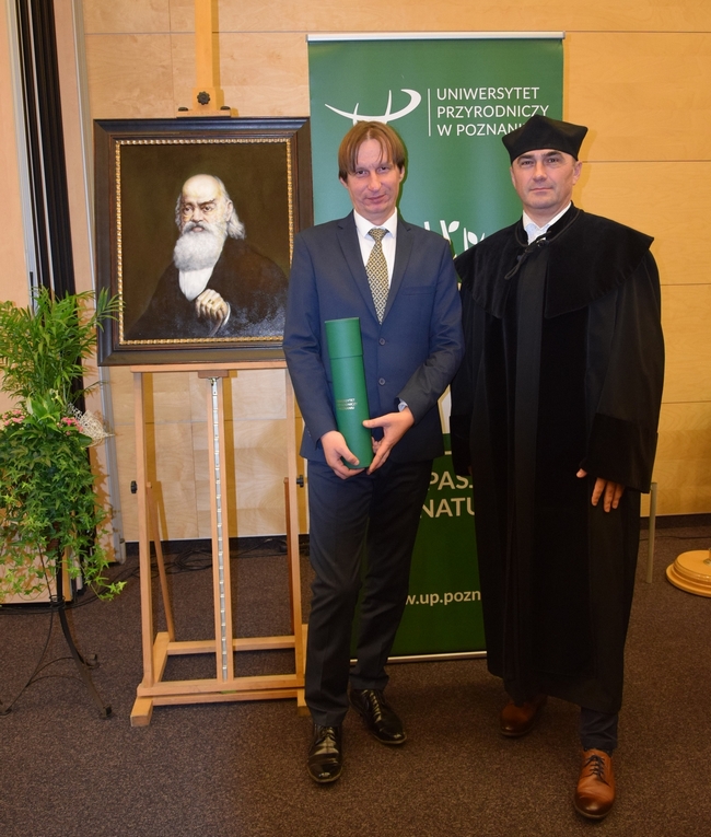 Daniel Krauklis i promotor pracy doktorskiej prof. dr hab. Piotr Szulc na tle loga UP w Poznaniu