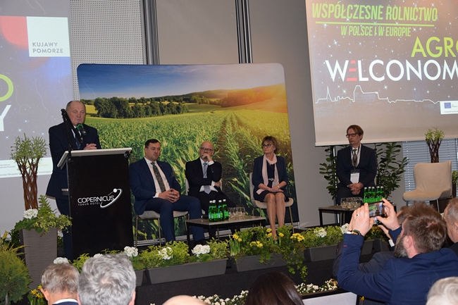 były Wiceminister Rolnictwa i Rozwoju Wsi Marek Sawicki, stojący na głównej scenie za mównicą, na dalszym pralnie pozostali prelegenci siedzący na fotelach 