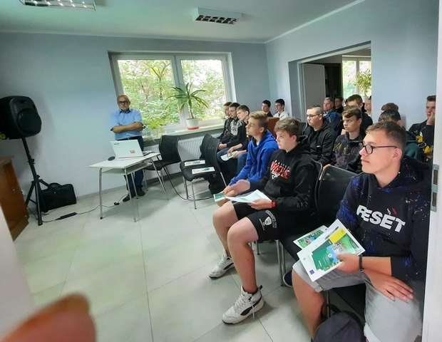 uczestnicy warsztatów stojący na polu, w tle budynki gospodarcze