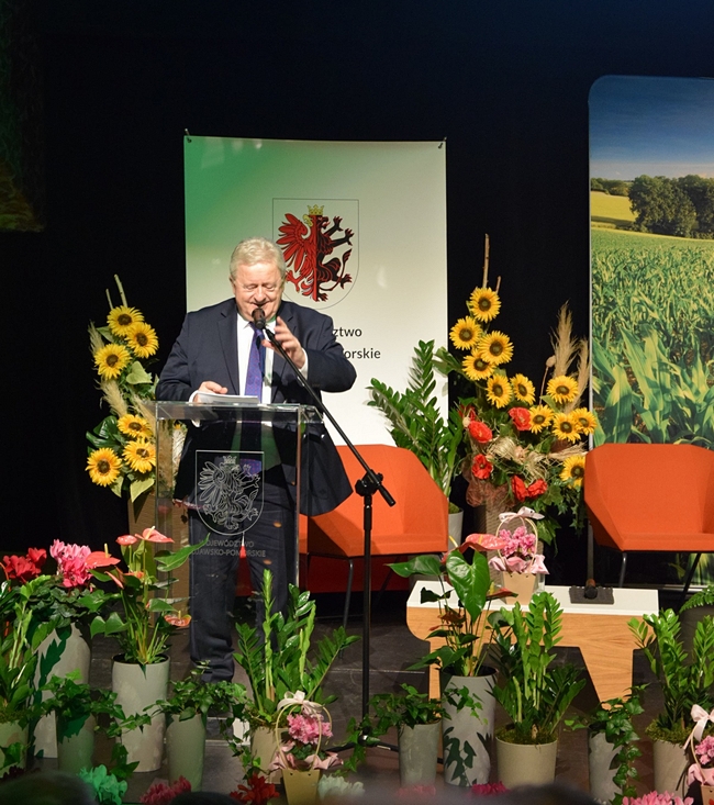 Minister Rolnictwa i Rozwoju Wsi podczas przemówienia, na scenie przyozdobionej w kwiaty