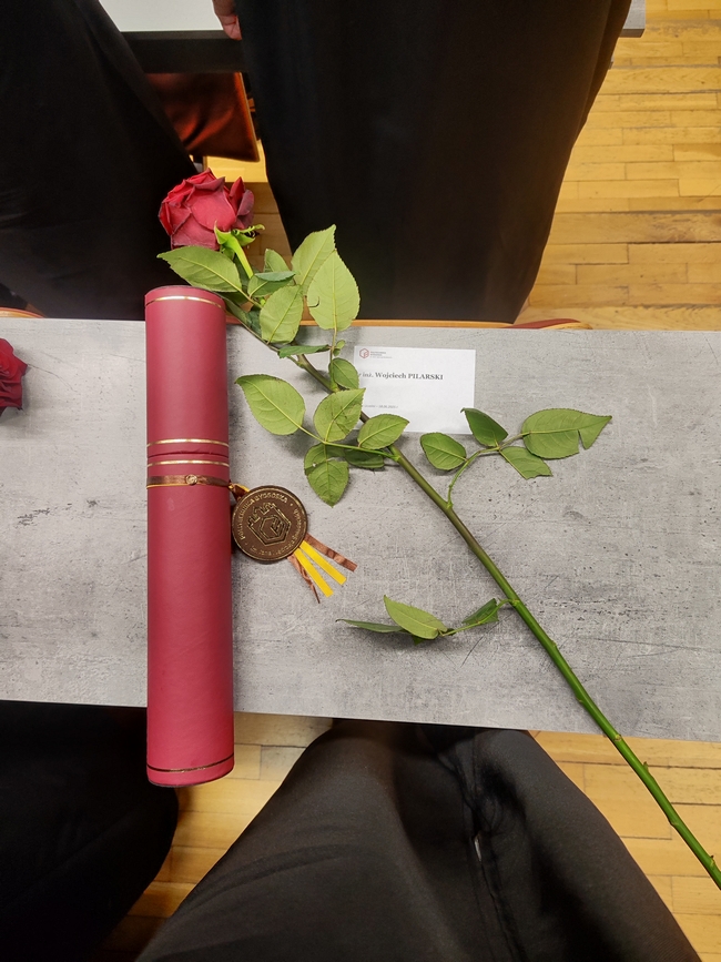 tuba z dyplomem i róża lezące na stoliku